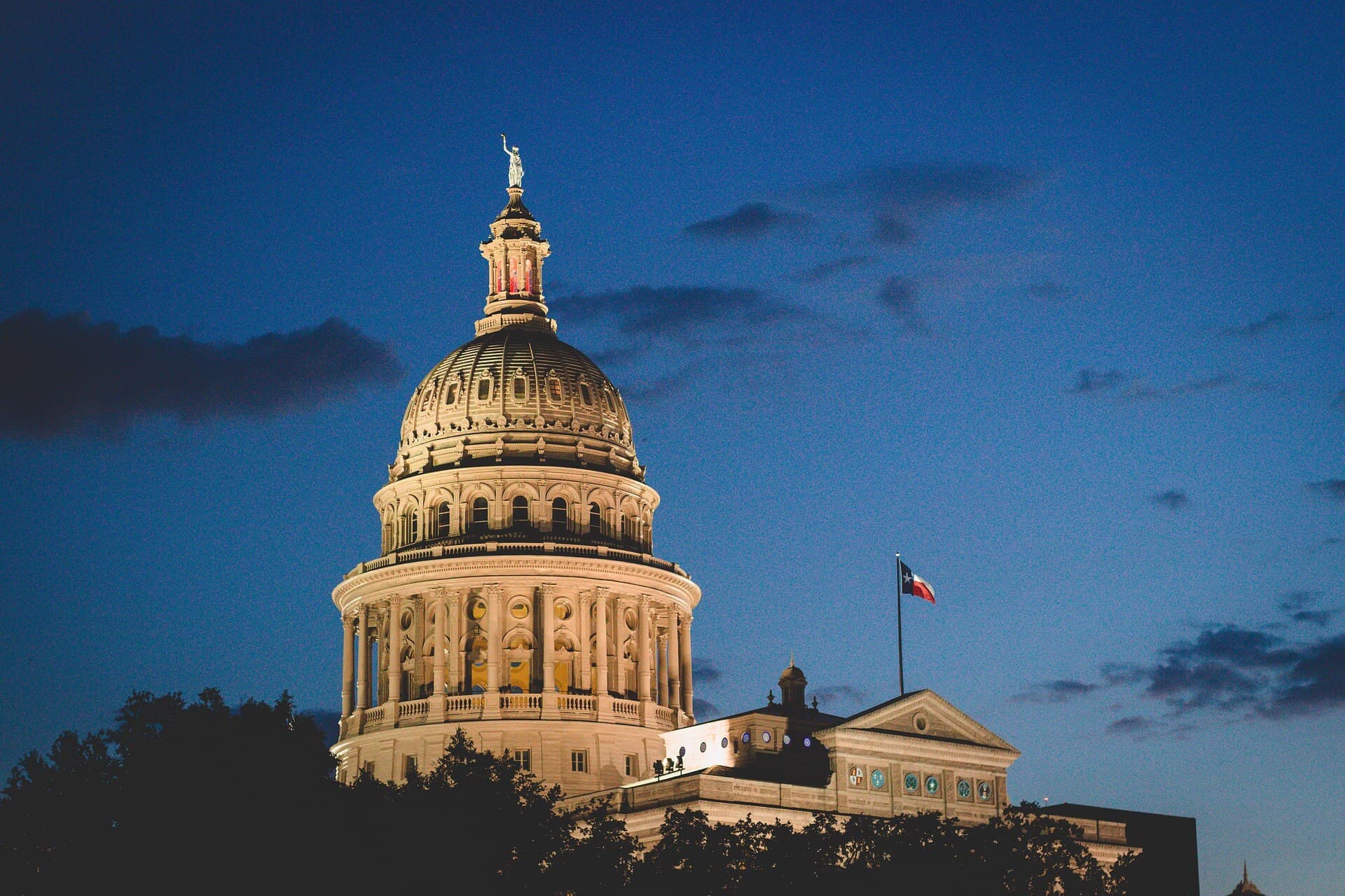 The Texas State Capitol dome lit gold against a deep blue Texas sky at dusk.