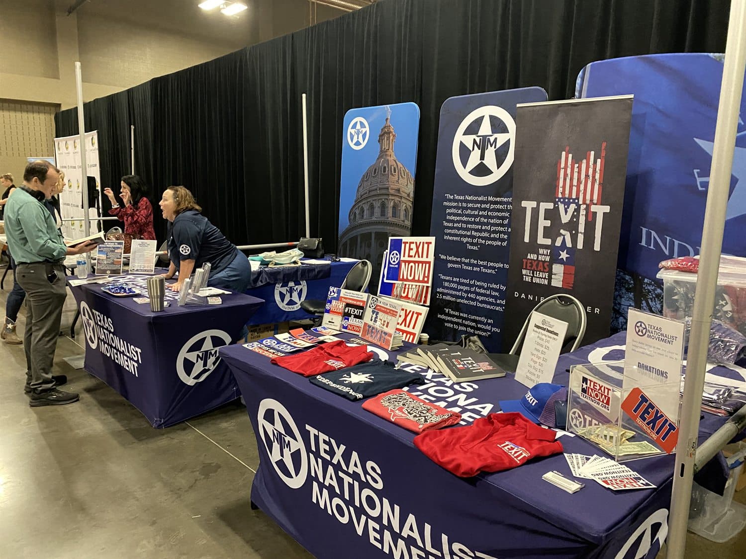 Texans staffing a Texas Nationalist Movement table of materials and merchandise at an indoor event.